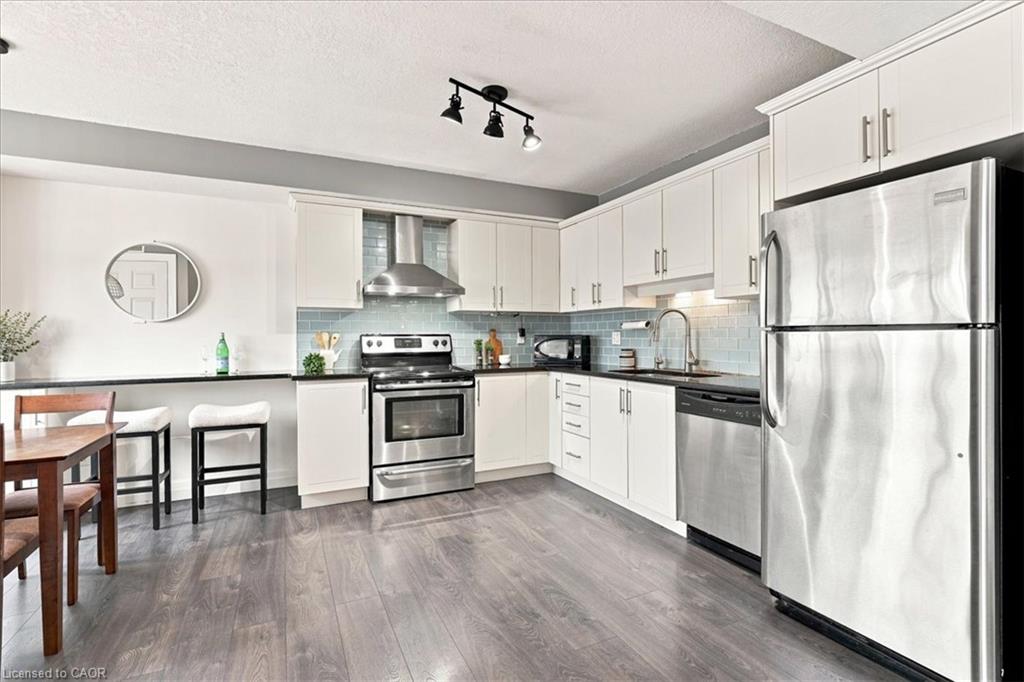 White cabinetry, stainless steel appliances, wood-finish flooring, black countertops, and a subway tile backsplash