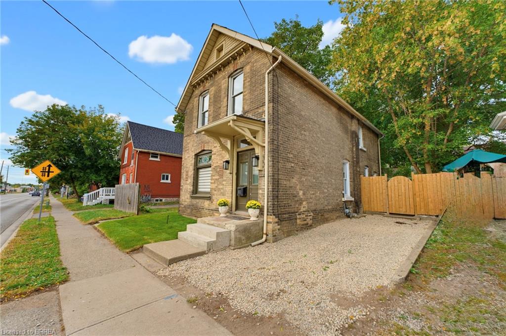 Brick exterior with decorative gables, covered entryway, concrete steps, gravel driveway, and wood fencing