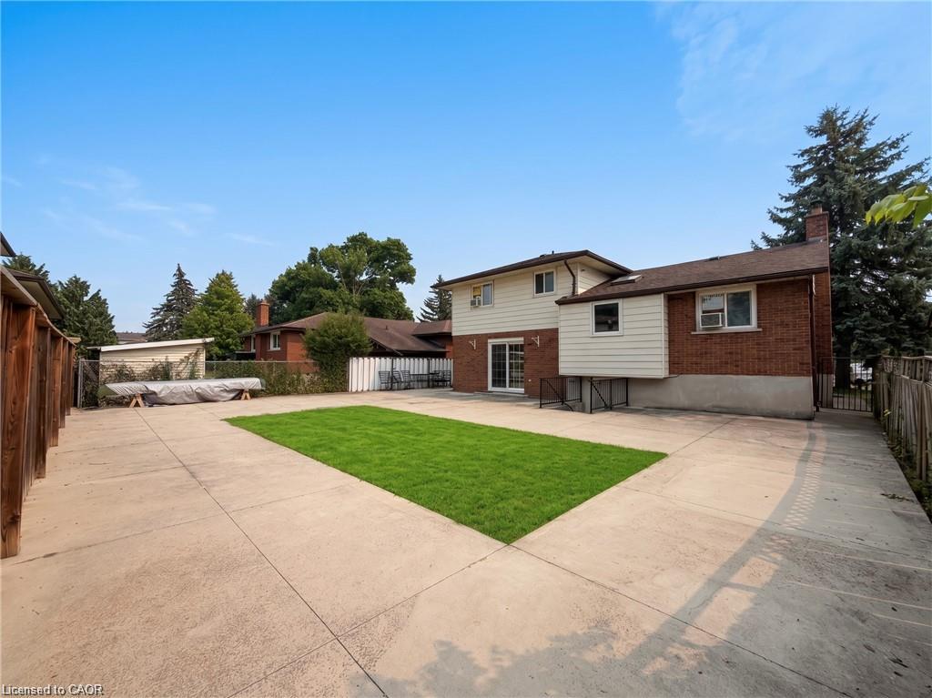 Expansive concrete patio with a central grass area, privacy fencing, and a brick and siding exterior