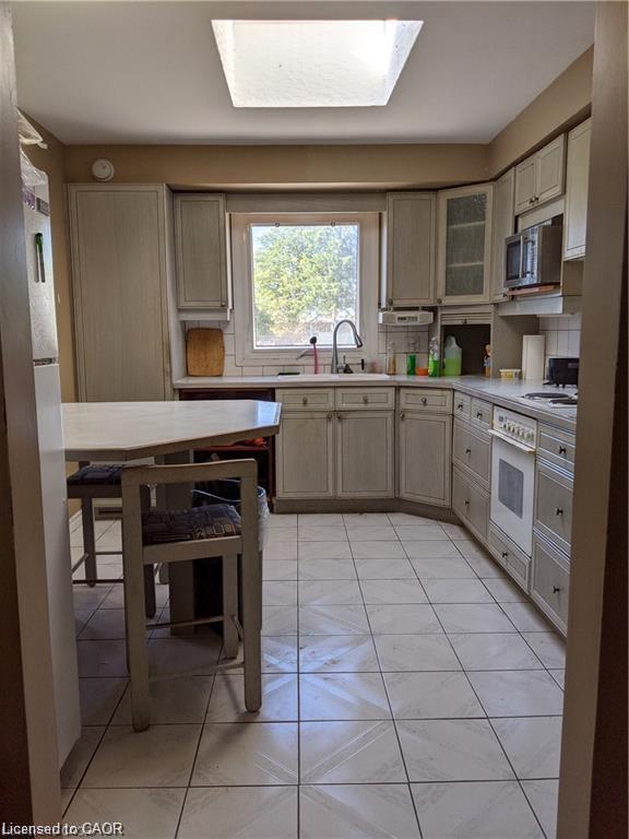 Skylight with a window, L-shaped cabinetry, built-in microwave, and tile flooring