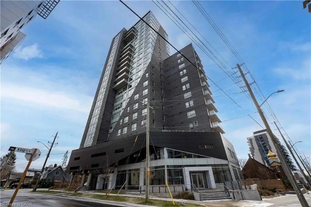 Modern high-rise building featuring a striking angular facade, extensive glass paneling, multiple balconies, and ground-level retail/commercial spaces