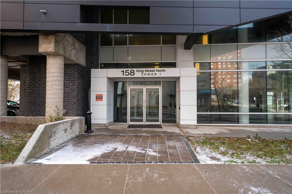 Modern building entrance featuring glass double doors, a white panel facade, dark brickwork, and concrete columns