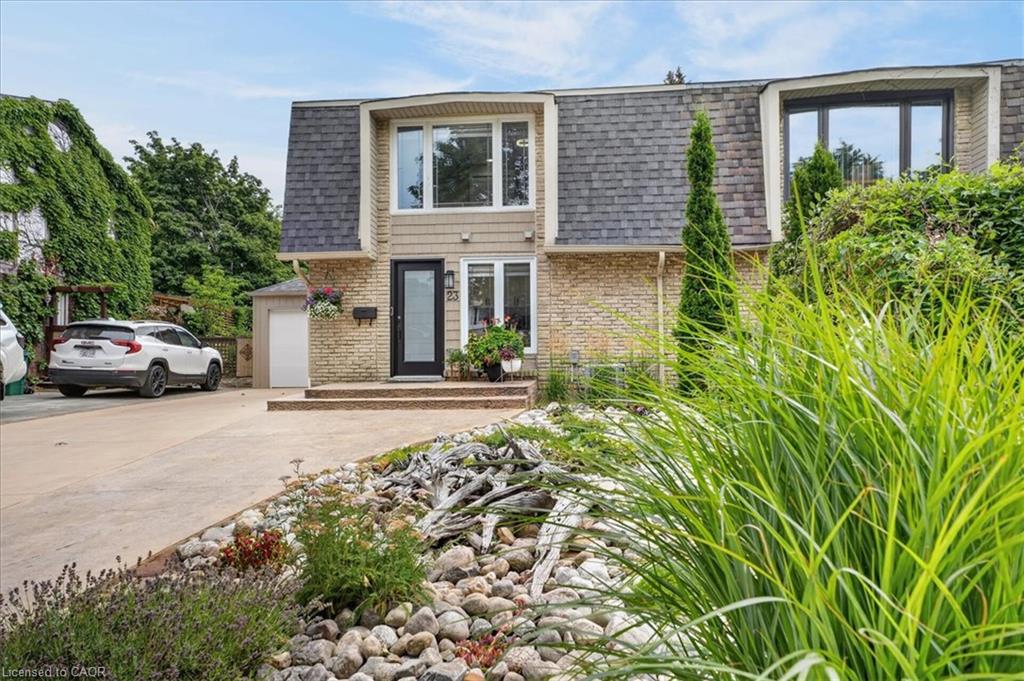Stone facade, dark-frame windows, front entry with transom window, dedicated garage, and a landscaped front garden