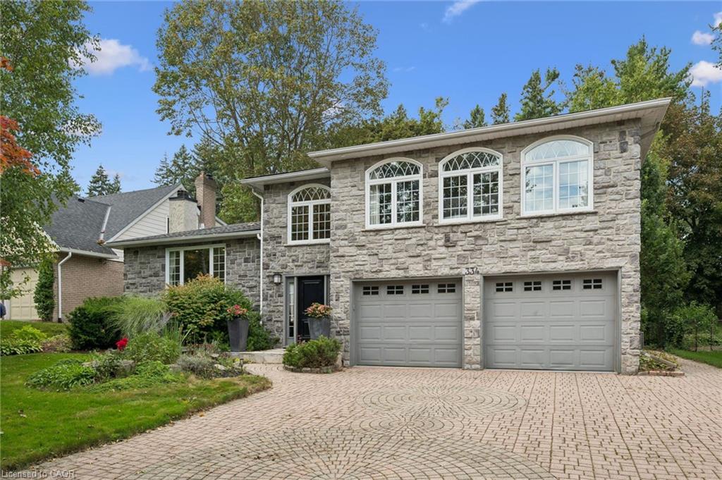 Stone facade with arched windows, an intricate paver driveway, and an attached two-car garage