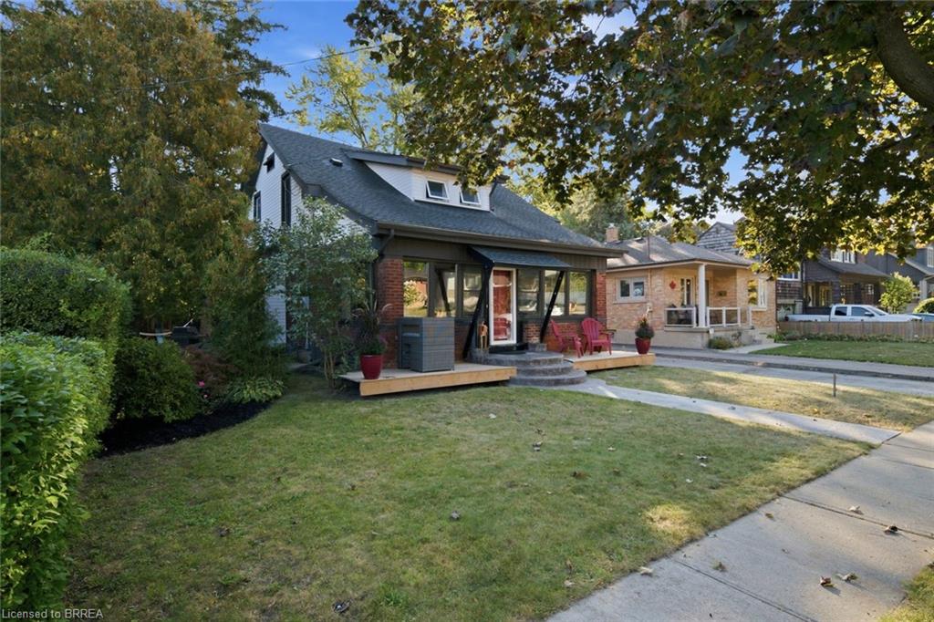 Brick and siding exterior with dormer windows, featuring a front lawn and a wood-finish deck with curved steps