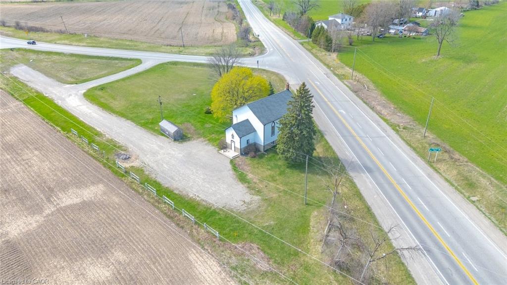 Rural property featuring a white building with dark roofing, extensive gravel parking area, mature trees