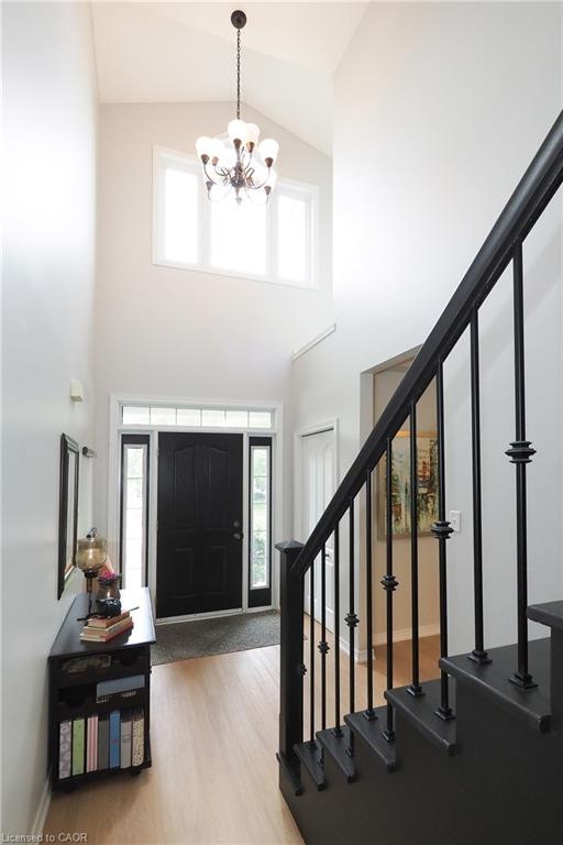 Double-height entryway with a decorative chandelier, light wood-finish flooring, and a black paneled door with sidelights