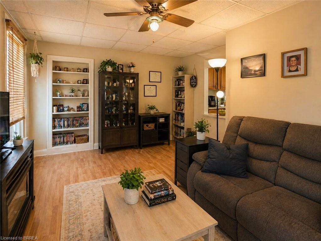 Living area featuring wood-finish flooring, a ceiling fan with integrated lighting, and a built-in bookshelf