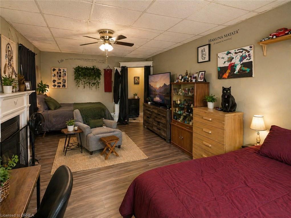 Spacious room featuring wood-finish flooring, a decorative fireplace mantel, and a ceiling fan with integrated lighting