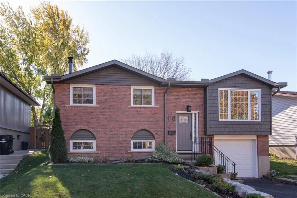 Split-level exterior featuring red brick facade, shake-style shingle siding, arched window detailing, attached single-car garage, and landscaped stone retaining walls