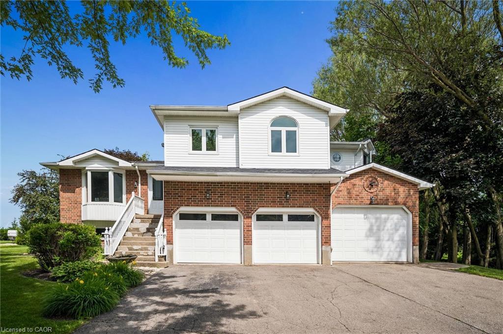 Split-level residence featuring a brick and white siding facade with a multi-car garage, bay window, and arched window details