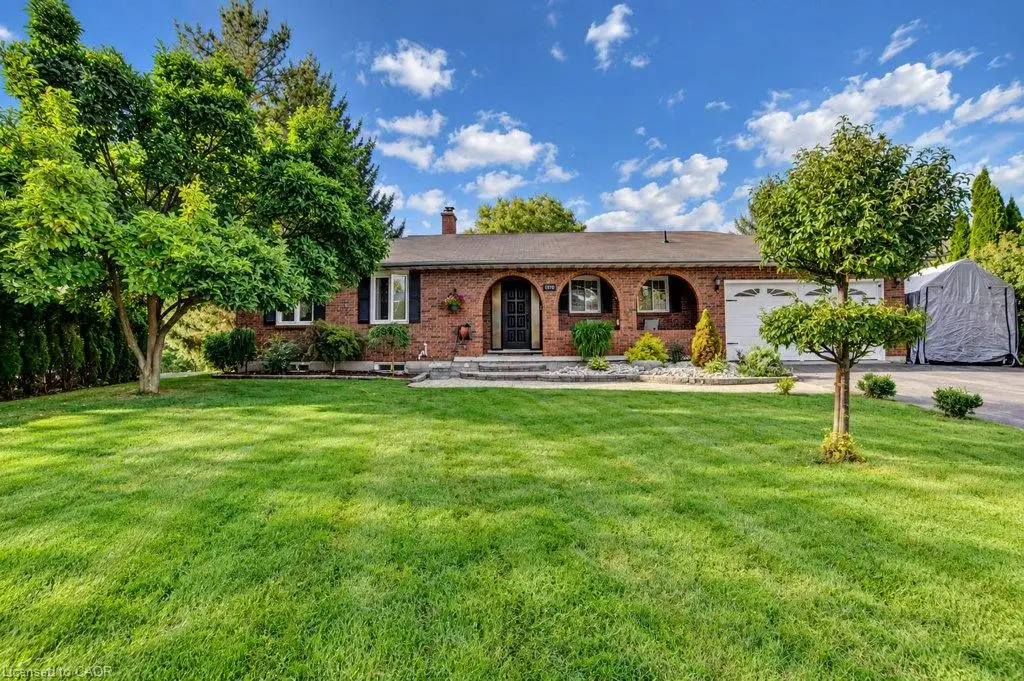 Brick exterior with arched entryway, attached garage, and mature landscaping