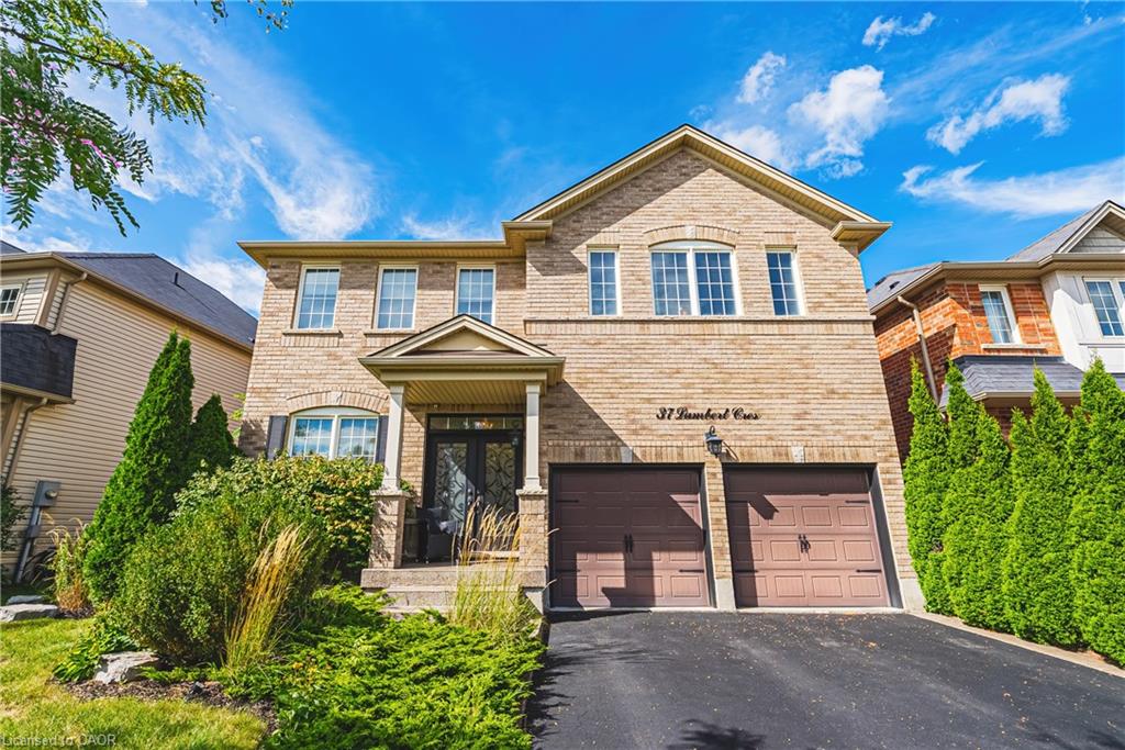 Brick exterior, covered front porch, double garage, paved driveway, and established landscaping