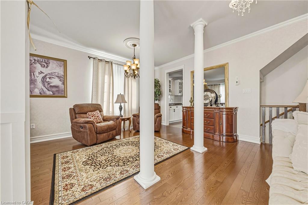 Hardwood flooring, crown molding, decorative columns, recessed ceiling medallion, and a chandelier with glass shades