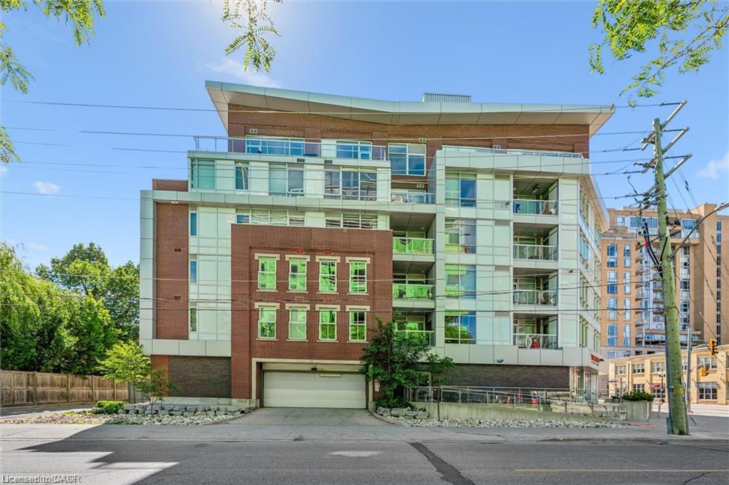 Contemporary multi-story building featuring a brick and glass facade, multiple balconies with clear railings, and a ground-level garage door