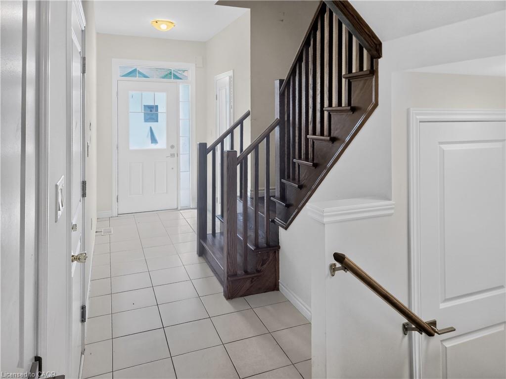 Bright foyer with ceramic tile flooring, a white paneled entry door with transom window, and a dark wood-finish staircase with matching handrail