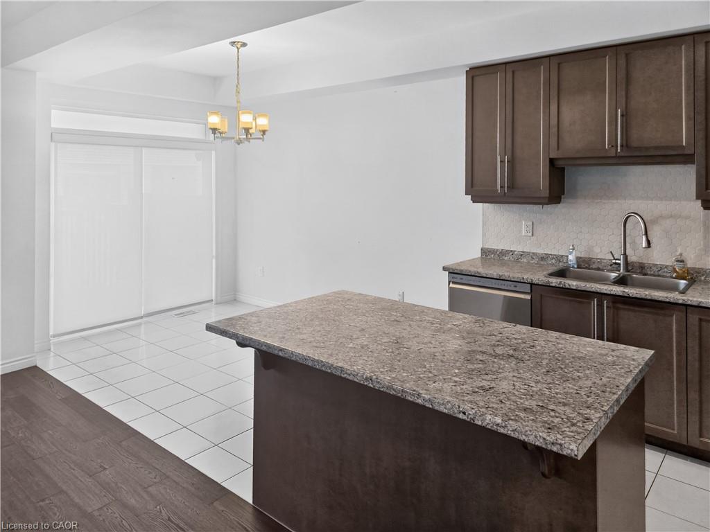 Kitchen island with extended countertop, wood-finish cabinetry, stainless steel dishwasher, and dual-basin sink with a gooseneck faucet