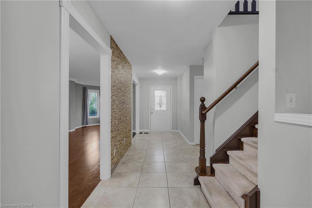 Foyer featuring light-toned tile flooring, a textured accent wall, and a wooden staircase with carpeted treads