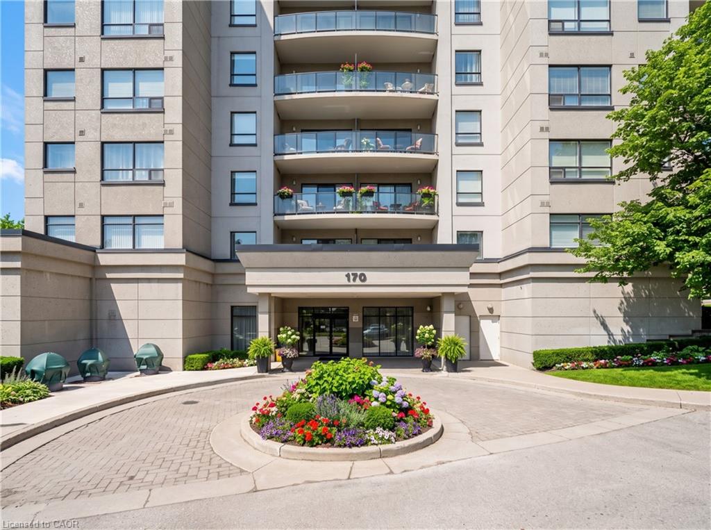Stone facade building with multiple balconies, a covered entrance, a paver stone circular driveway, and a central landscaped garden