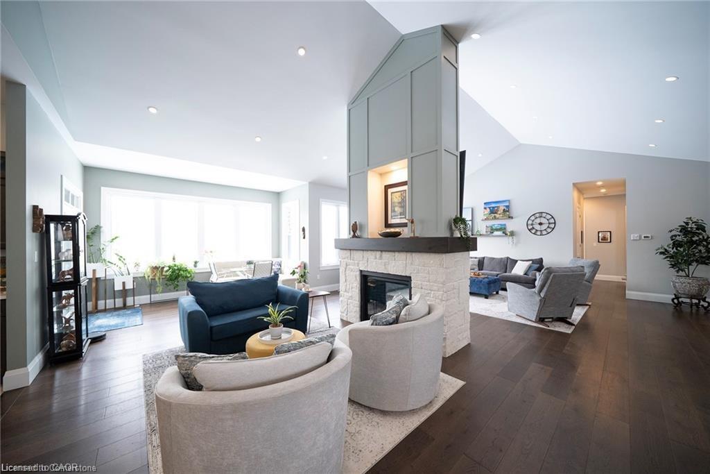 Spacious living area featuring a central white brick fireplace with a wood-finish mantel, vaulted ceilings, recessed lighting, and rich wood-finish flooring
