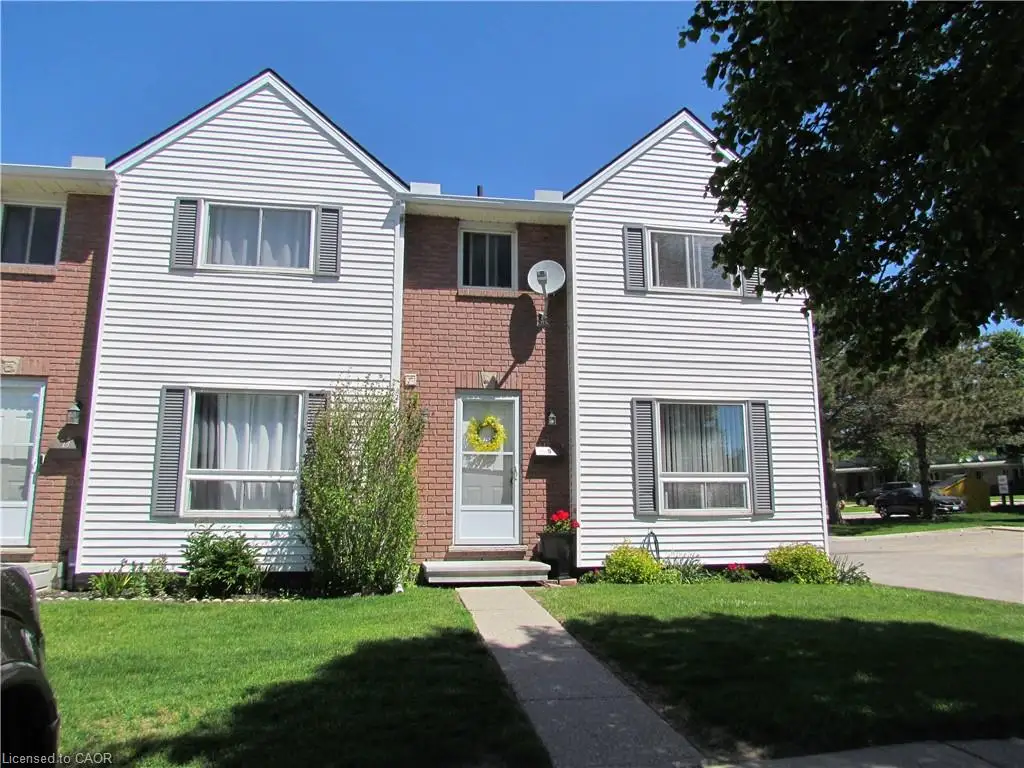 Townhome exterior featuring white siding, brick accents, gray window shutters, and a central entrance with a small porch