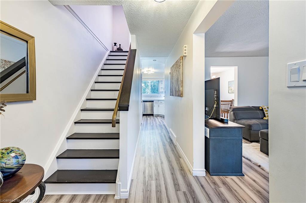 Modern open-concept entryway featuring a striking floating staircase with dark treads and metal railings, wide-plank wood-finish flooring throughout, and bright natural light from front-facing windows