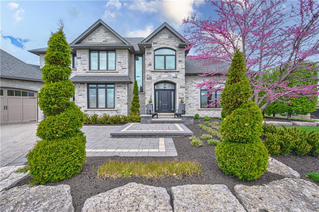 Stone facade, arched entry, paver driveway, tiered landscaping, and architectural windows