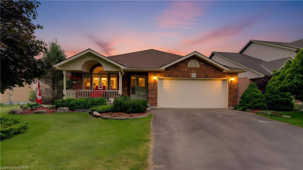 Brick-front residence featuring a covered front porch, an arched window, and a prominent attached garage with a paved driveway