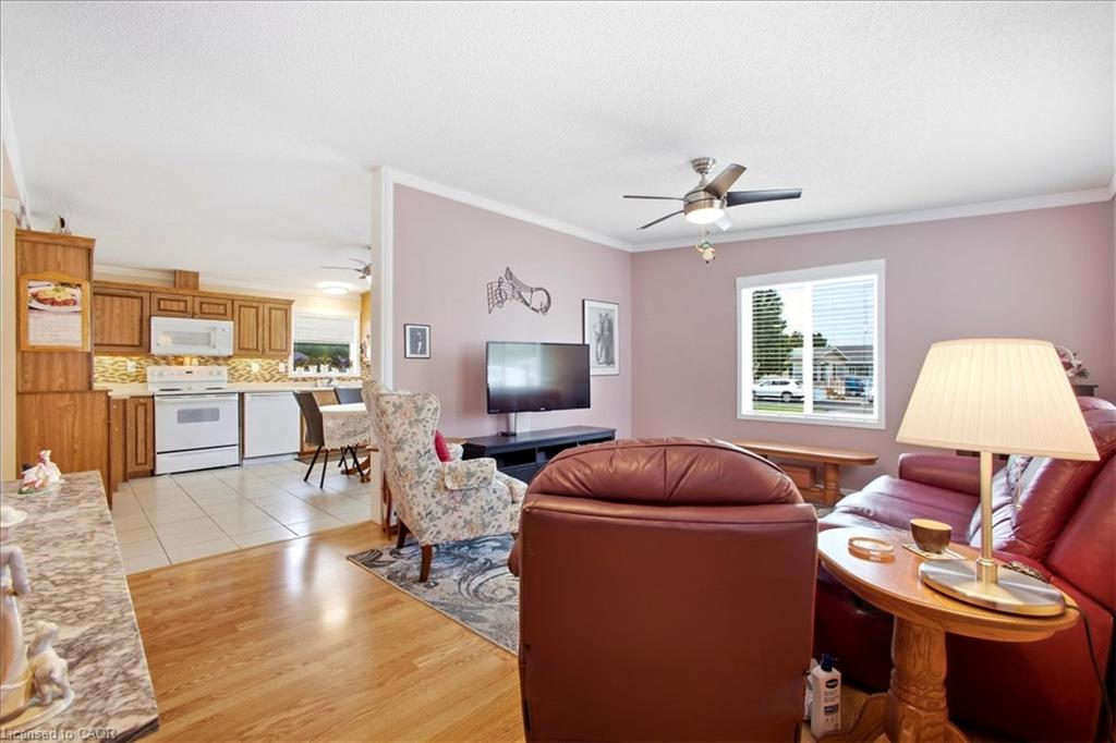 Open-concept living area featuring wood-finish flooring, a ceiling fan, and crown molding