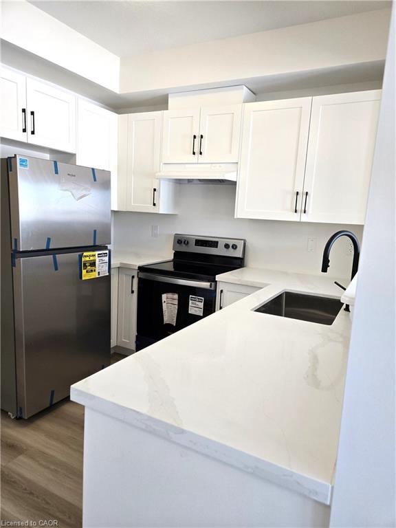 Contemporary kitchen featuring white cabinetry with black hardware, stainless steel appliances, white countertops, and wood-finish flooring