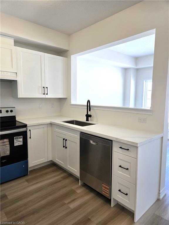 Modern kitchen featuring white shaker cabinetry, stainless steel sink with a matte black faucet, and durable wood-finish flooring