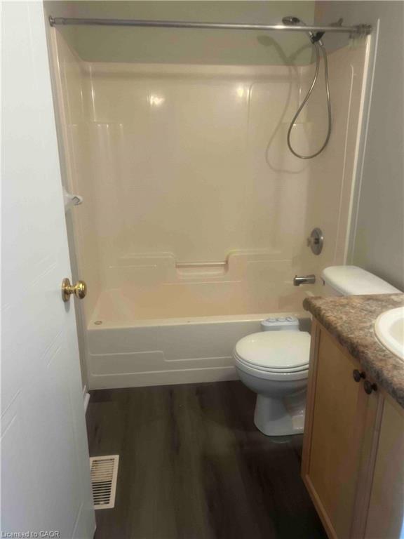 Bathroom featuring a white tub/shower combination, dark wood-finish flooring, a toilet, a light wood vanity with a light-colored countertop, and a white sink