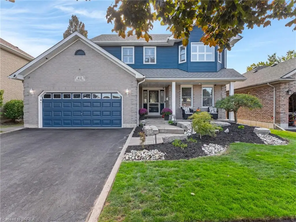 Two-story residence featuring light gray brick and blue siding, a covered front porch with white columns, an attached garage with a blue door, a paved driveway, and landscaped front yard