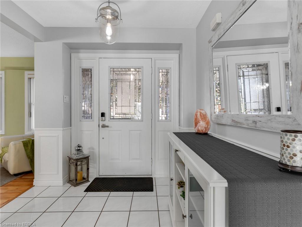 White tile flooring, wainscoting detail, front entry door with decorative glass inserts, and a clear glass pendant light fixture