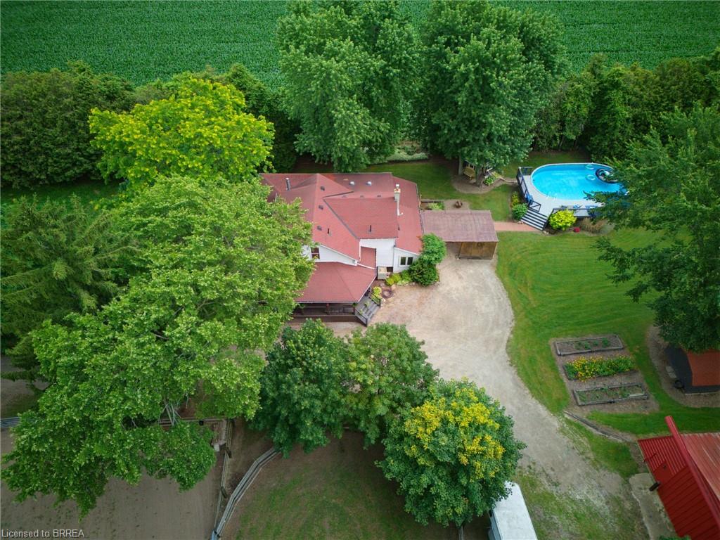 Expansive property featuring a red-roofed residence, a large above-ground pool with surrounding decking, a gravel driveway, and multiple cultivated garden beds