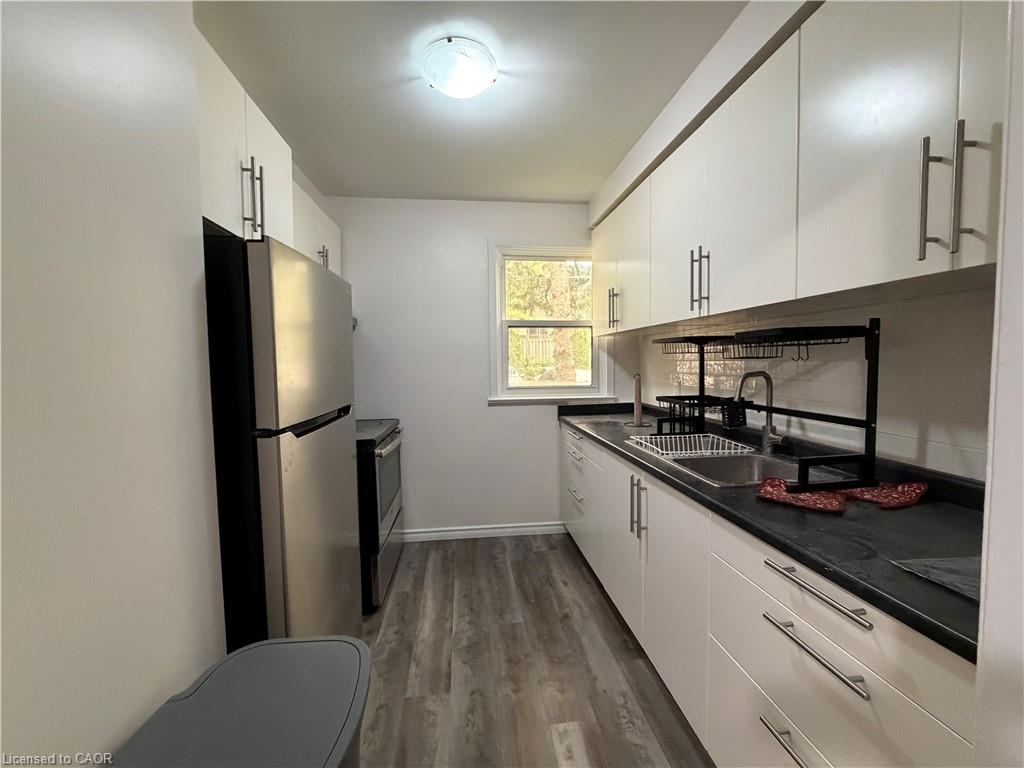 Galley kitchen featuring white cabinetry with silver-tone hardware, dark countertops, and  Vinyl Plank flooring