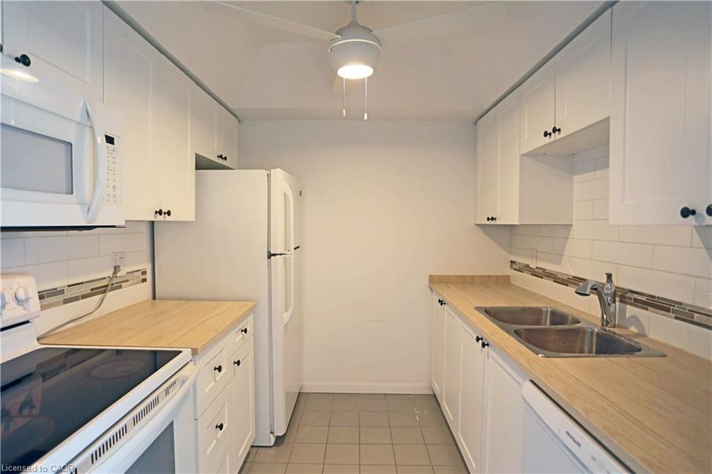 Kitchen with backsplash, white appliances, white cabinetry, light countertops, and light tile patterned floors