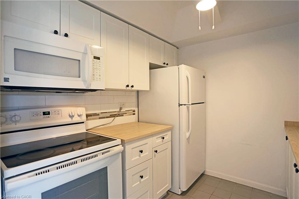 Kitchen featuring white appliances, white cabinetry, backsplash, light countertops, and light tile patterned floors