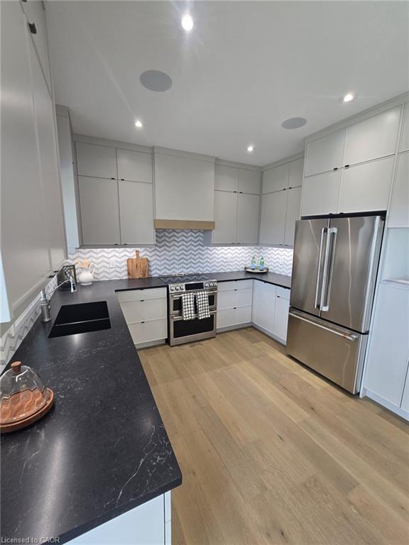 Modern kitchen featuring light gray cabinetry, dark countertops with subtle veining, and a chevron tile backsplash