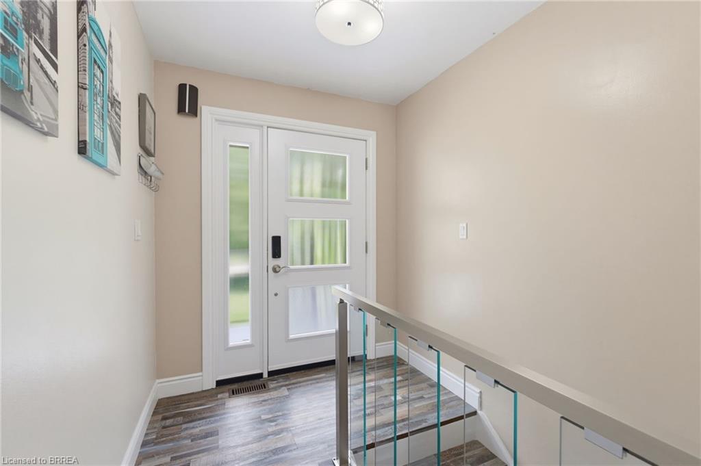 Entryway featuring a contemporary white door with frosted glass panels, wood-finish flooring, a ceiling-mounted light fixture, and a modern stair railing with glass inserts