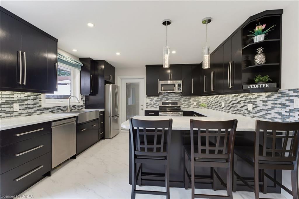 Modern kitchen featuring dark cabinetry, stainless steel appliances, a white stone countertop, and a mosaic tile backsplash