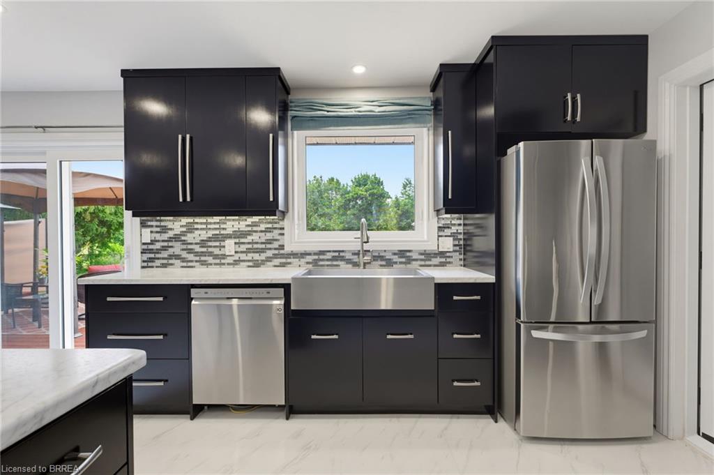 Modern kitchen featuring dark cabinetry with brushed nickel hardware, white countertops, and a full suite of stainless steel appliances