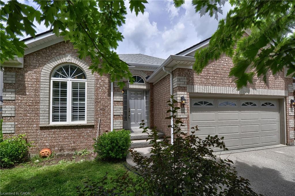Brick exterior featuring a two-car garage with arched window inserts, an arched entry window with louvered shutters, a gray front door, and mature landscaping