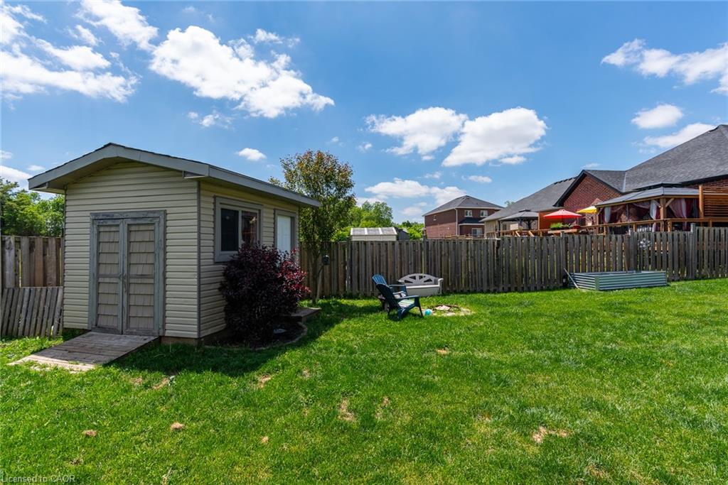 Expansive green lawn with a wooden privacy fence, featuring a storage shed with double doors and window, and a raised garden bed