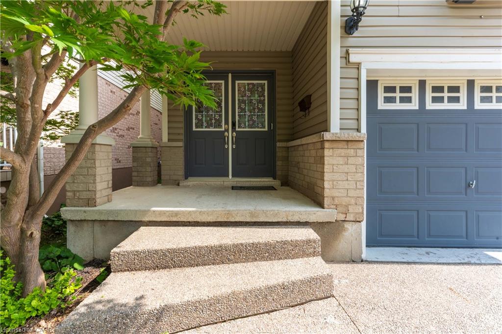 Double entry doors with decorative glass inserts, concrete steps, brick facade accents, and an attached garage with window inserts