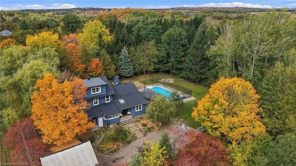 Multi-level residence with dark-toned vertical siding, an inground pool, stone hardscaping, and extensive mature tree coverage