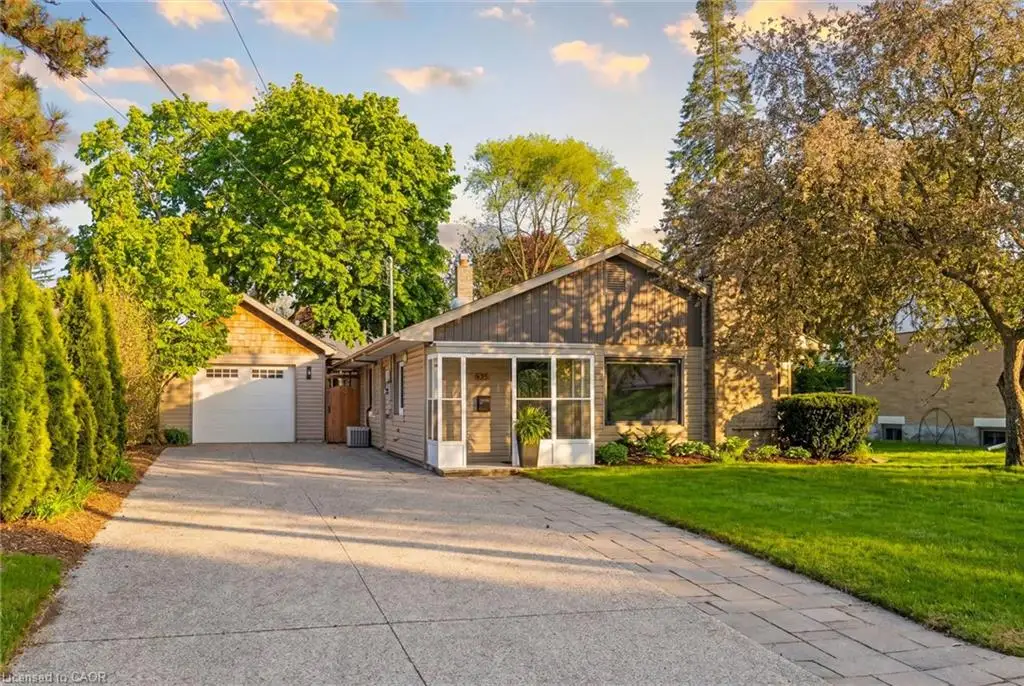 Concrete driveway with paver stone accents, attached garage with a white door, enclosed front porch, and mature trees surrounding the property