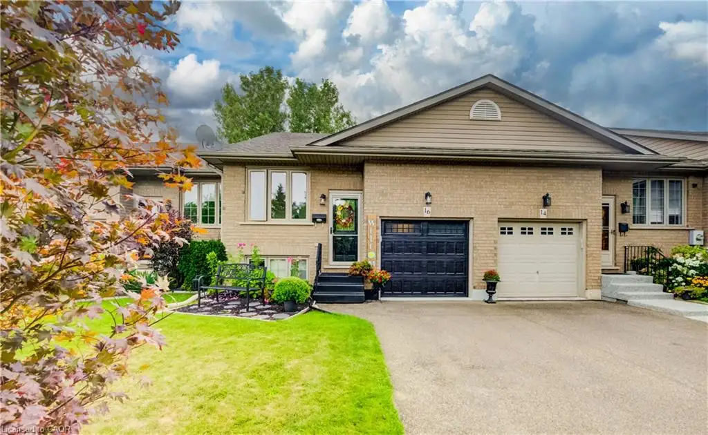 Brick exterior with a peaked roofline, attached garage, paved driveway, and manicured landscaping