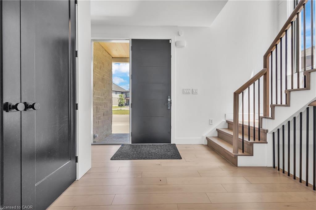 Hardwood flooring, light wood staircase with black iron spindles, white walls, and a contemporary entry door