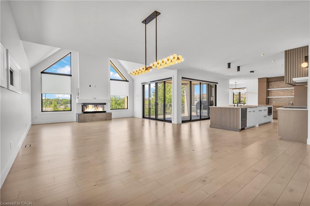 High vaulted ceiling, wood-finish flooring, linear fireplace with concrete hearth, sliding glass doors, and a modern island with built-in appliances